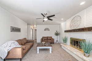 Living room featuring carpet, a textured ceiling, ceiling fan, and a fireplace