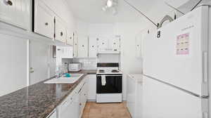 Kitchen with decorative backsplash, sink, white cabinetry, white appliances, and dark stone countertops