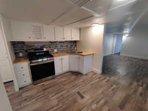 Kitchen featuring dark wood-type flooring, white cabinets, sink, stainless steel range, and tasteful backsplash