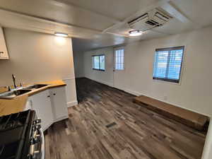 Kitchen with sink, butcher block countertops, white cabinets, stainless steel gas stove, and dark hardwood / wood-style floors