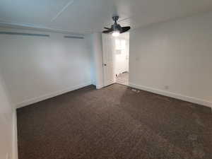 Spare room with ceiling fan and dark colored carpet