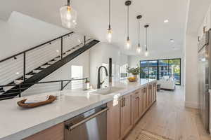 Kitchen featuring light stone countertops, hanging light fixtures, sink, light hardwood / wood-style floors, and stainless steel dishwasher