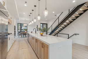 Kitchen featuring pendant lighting, white cabinets, a spacious island, light wood-type flooring, and light brown cabinetry