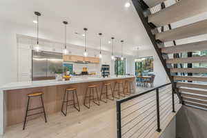 Kitchen with light wood-type flooring, appliances with stainless steel finishes, pendant lighting, a kitchen breakfast bar, and a spacious island