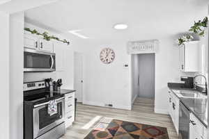 Kitchen with white cabinets, sink, light wood-type flooring, and appliances with stainless steel finishes