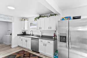 Kitchen with light hardwood / wood-style flooring, white cabinets, sink, and stainless steel appliances