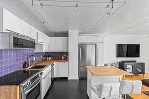 Kitchen featuring wooden counters, white cabinets, sink, tasteful backsplash, and appliances with stainless steel finishes