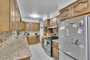 Kitchen with decorative backsplash, appliances with stainless steel finishes, sink, and light tile patterned floors