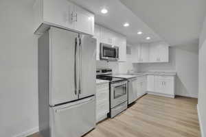 Kitchen featuring white cabinetry, appliances with stainless steel finishes, light wood-type flooring, light stone countertops, and sink