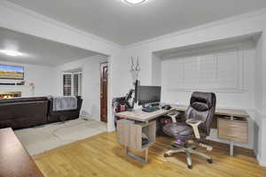 Office area with a fireplace, light hardwood / wood-style flooring, and crown molding