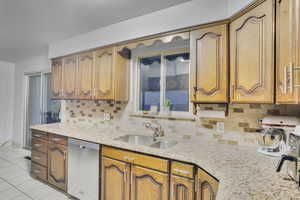 Kitchen featuring stainless steel dishwasher, light stone counters, sink, and backsplash