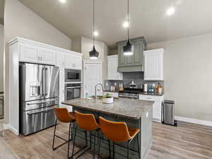 Kitchen featuring white cabinetry, light wood-type flooring, appliances with stainless steel finishes, and a center island with sink