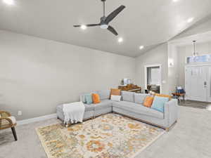 Carpeted living room featuring high vaulted ceiling and ceiling fan with notable chandelier