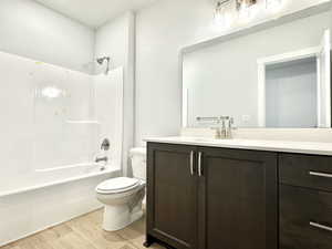 Full bathroom featuring vanity, wood-type flooring, washtub / shower combination, and toilet