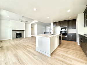 Kitchen with light hardwood / wood-style floors, a tiled fireplace, sink, a kitchen island with sink, and appliances with stainless steel finishes