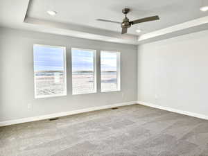 Carpeted spare room with ceiling fan and a raised ceiling