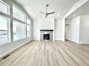 Unfurnished living room with a textured ceiling, a tile fireplace, high vaulted ceiling, ceiling fan, and light hardwood / wood-style flooring