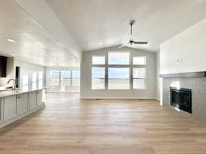 Unfurnished living room with ceiling fan with notable chandelier, light wood-type flooring, and vaulted ceiling