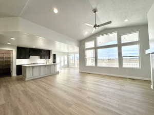 Unfurnished living room with ceiling fan with notable chandelier, a textured ceiling, sink, and light hardwood / wood-style flooring