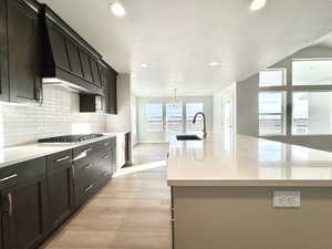 Kitchen featuring stainless steel gas cooktop, a center island with sink, sink, and premium range hood