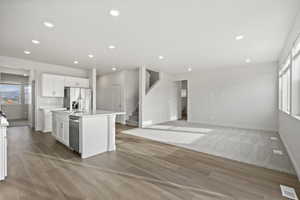 Kitchen with white cabinets, plenty of natural light, an island with sink, and stainless steel appliances