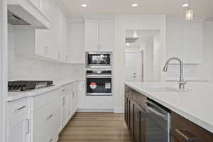 Kitchen featuring dark brown cabinetry, white cabinetry, premium range hood, light hardwood / wood-style floors, and appliances with stainless steel finishes