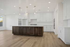 Kitchen with a center island with sink, white cabinetry, and light wood-type flooring