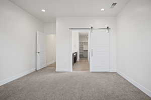 Unfurnished bedroom featuring a closet, a walk in closet, a barn door, and light colored carpet