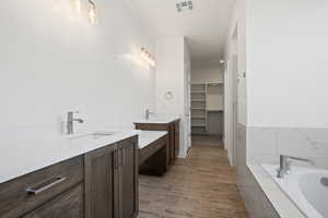 Bathroom with tiled tub, vanity, and wood-type flooring