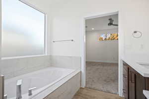 Bathroom featuring vanity, hardwood / wood-style floors, a relaxing tiled tub, and ceiling fan