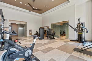 Exercise room with a tray ceiling, ceiling fan, and a towering ceiling