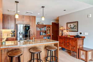 Kitchen with tasteful backsplash, light wood-type flooring, pendant lighting, stainless steel refrigerator with ice dispenser, and light stone countertops