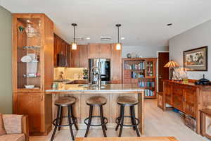 Kitchen with stainless steel appliances, sink, hanging light fixtures, light wood-type flooring, and decorative backsplash