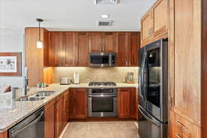 Kitchen featuring light stone counters, stainless steel appliances, hanging light fixtures, sink, and kitchen peninsula