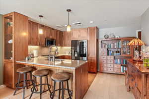 Kitchen with stainless steel appliances, kitchen peninsula, hanging light fixtures, light stone countertops, and light hardwood / wood-style flooring