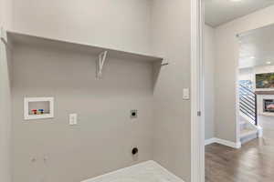 Main level laundry room featuring electric dryer hookup, washer hookup, a textured ceiling, and wood-type flooring