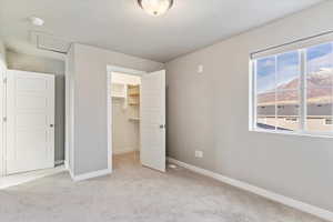 Unfurnished bedroom featuring a walk in closet, a closet, light colored carpet, and a textured ceiling