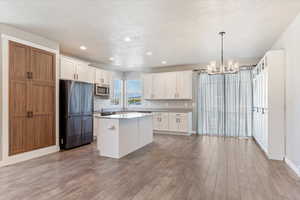 Kitchen with white cabinets, appliances with stainless steel finishes, a center island, and light hardwood / wood-style floors