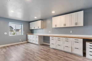 Desirable craft room (or bedroom) featuring white cabinetry, light wood-type flooring, and a textured ceiling