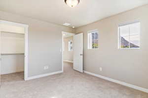 Unfurnished bedroom with light carpet, a spacious closet, and a closet