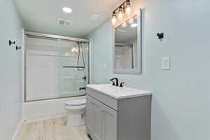 Full bathroom featuring toilet, vanity, wood-type flooring, and combined bath / shower with glass door