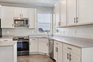 Kitchen with stainless steel appliances, white cabinetry, light hardwood / wood-style floors, induction range