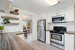 Kitchen featuring tasteful backsplash, light hardwood / wood-style flooring, white cabinets, and appliances with stainless steel finishes