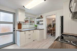 Kitchen with stainless steel fridge, white cabinetry, light hardwood / wood-style flooring, and range