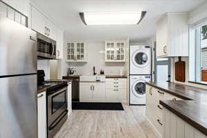 Kitchen with stacked washer / drying machine, white cabinets, and stainless steel appliances