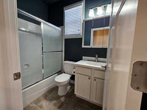 Full bathroom with tile patterned flooring, vanity, enclosed tub / shower combo, and toilet