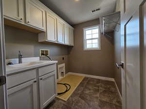 Washroom with sink, cabinets, washer hookup, electric dryer hookup, and dark tile patterned flooring