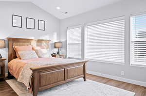 Bedroom with light hardwood / wood-style floors, vaulted ceiling, and multiple windows