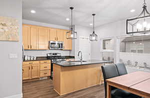 Kitchen featuring dark hardwood / wood-style flooring, hanging light fixtures, a kitchen island with sink, and stainless steel appliances