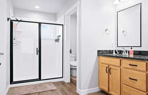 Bathroom with toilet, vanity, a shower with door, and hardwood / wood-style flooring